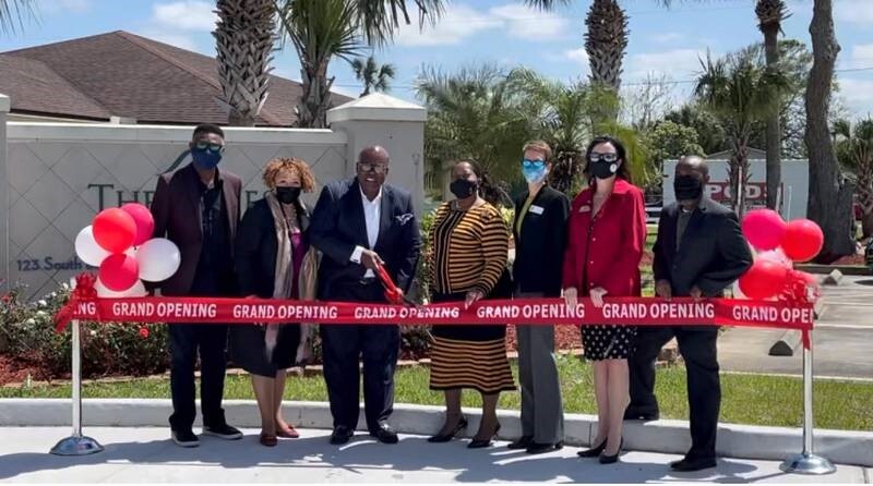 Group of people in front of sign cutting a ribbon