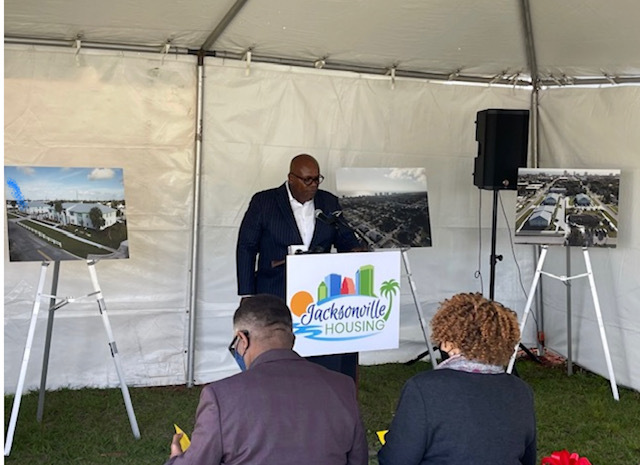 Man at podium speaking to group under tent