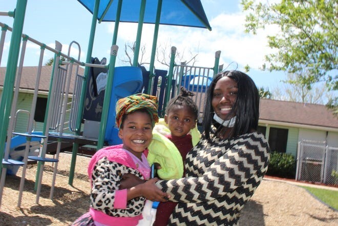 mom smiling at camera with 2 kids outside of residence